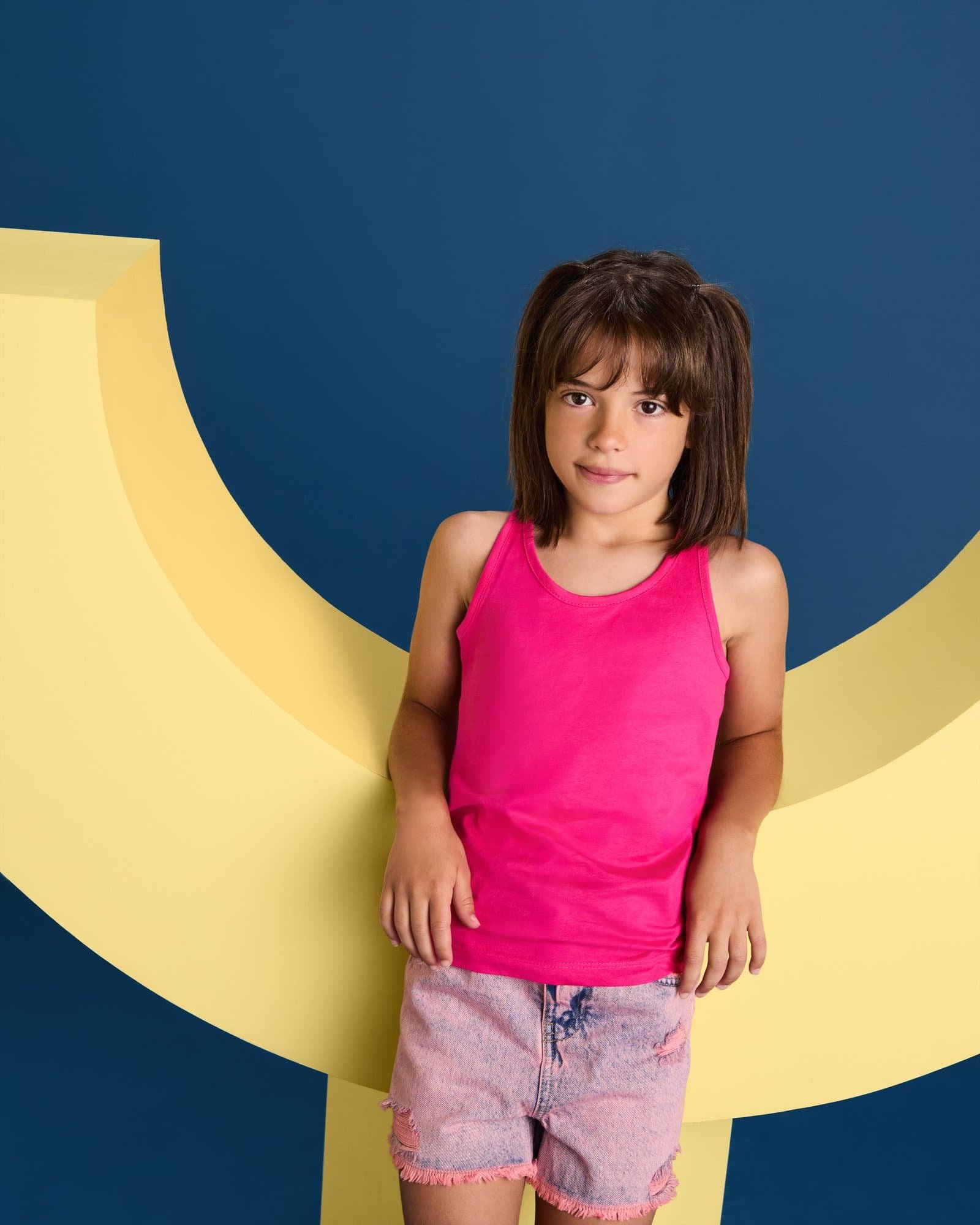 MUGYNOX - Mujer con camiseta rosa y pantalones beige en estudio Niña con camiseta rosa y pantalones cortos en un fondo colorido, ideal para moda infantil y estilo j.